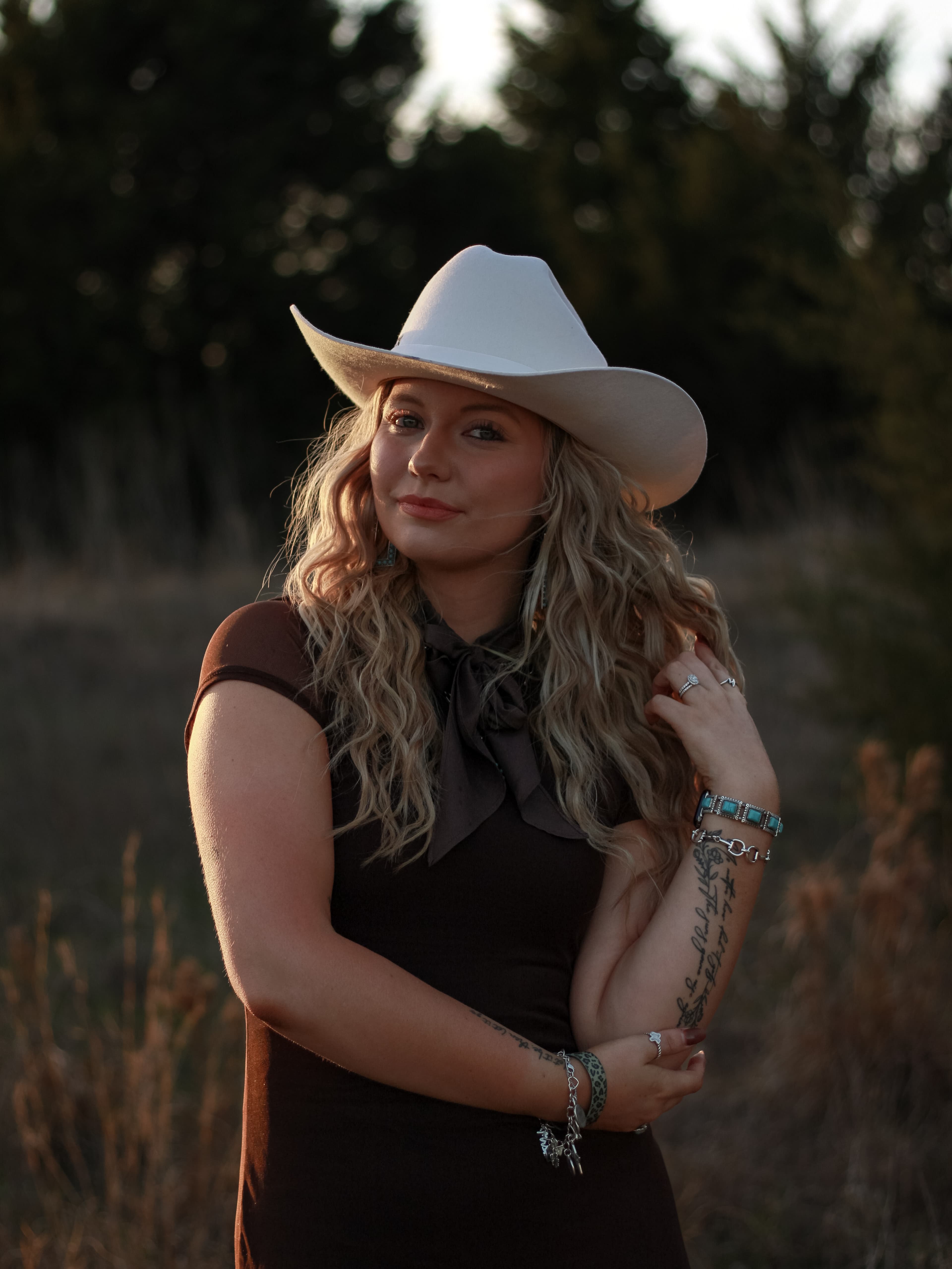 A woman in a white cowboy hat standing in warm evening light.