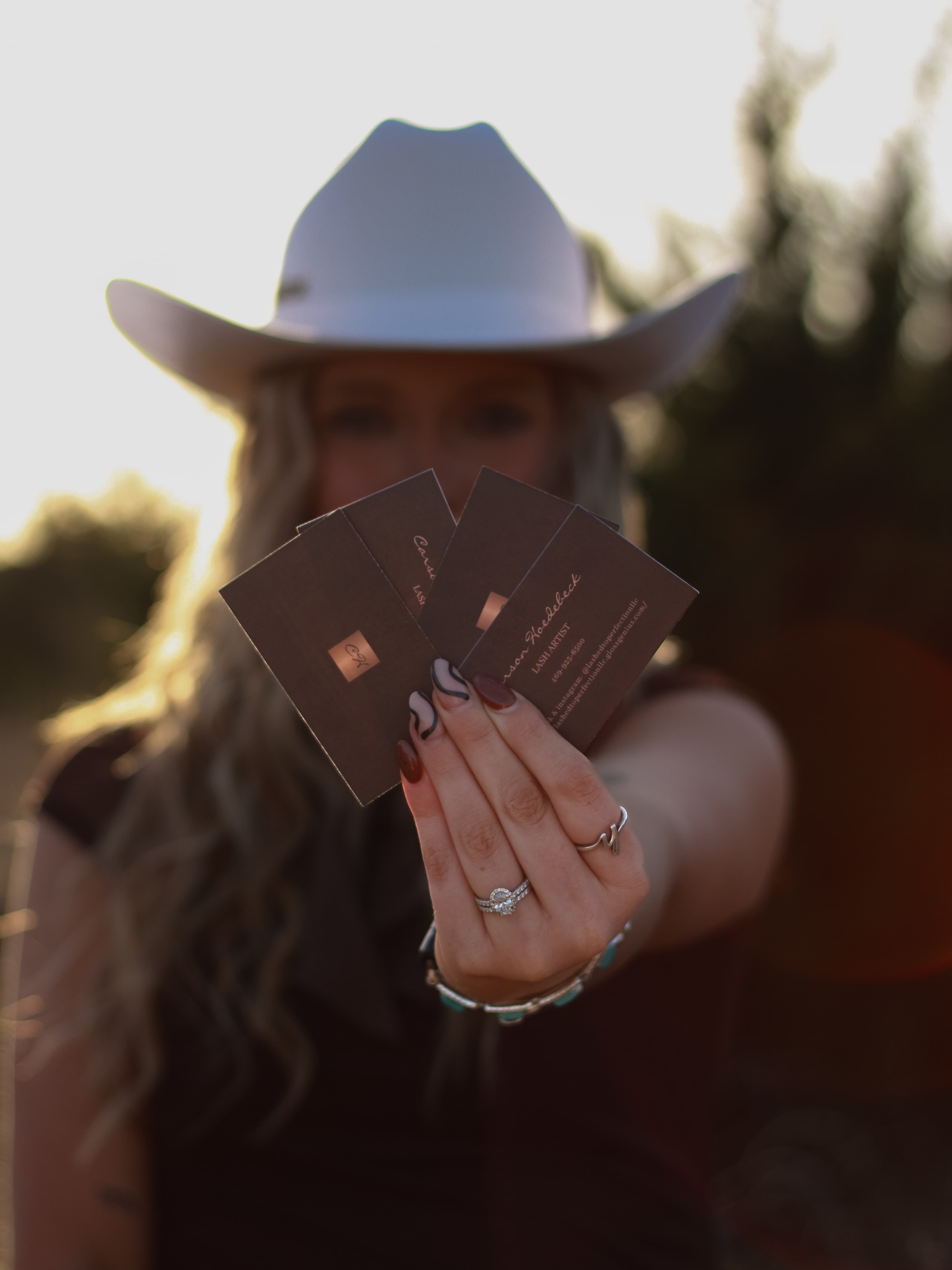 A woman in a white cowboy hat holding a fan of cards toward the camera.