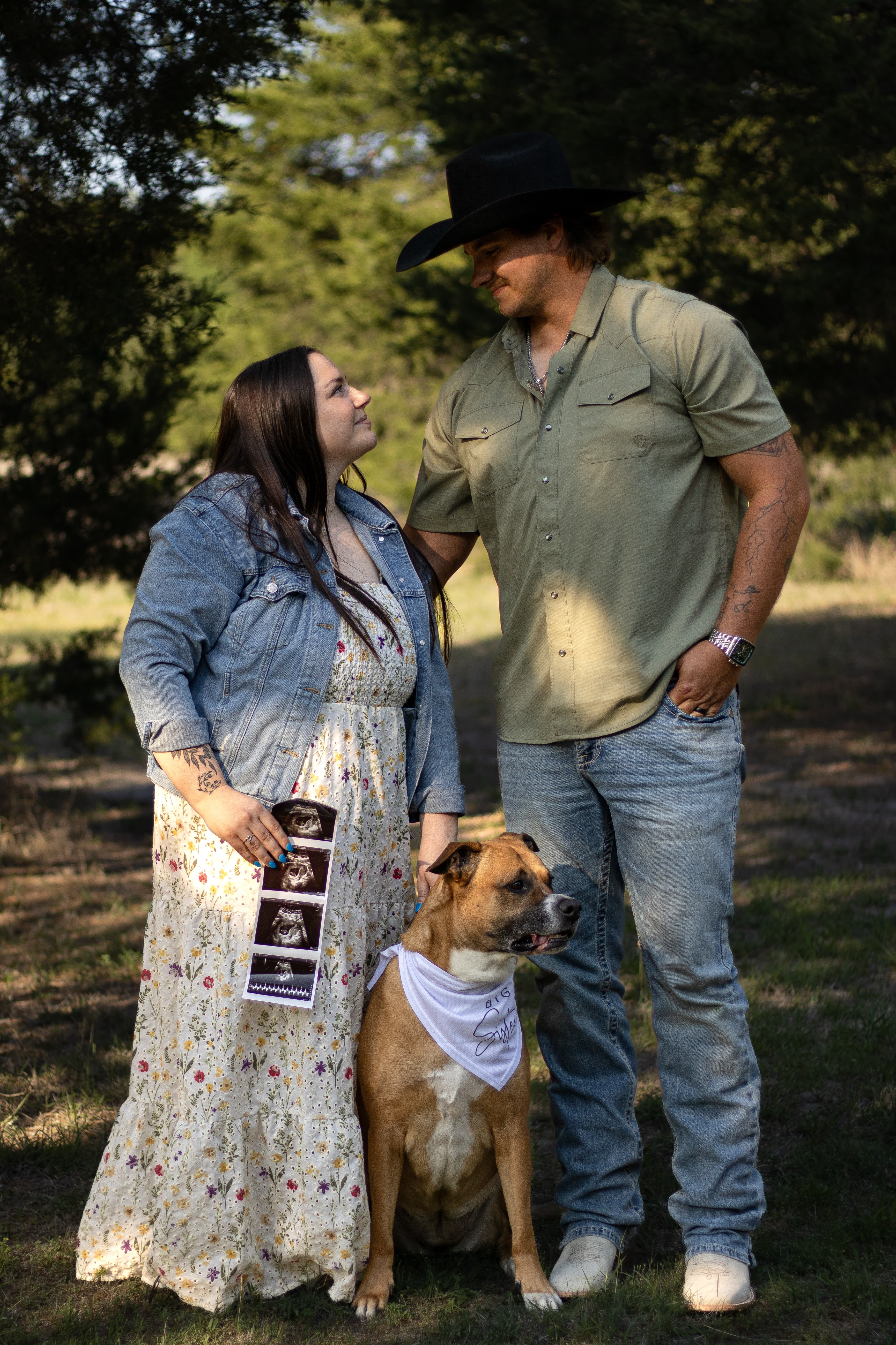 An expectant couple looking at each other with their dog seated between them.