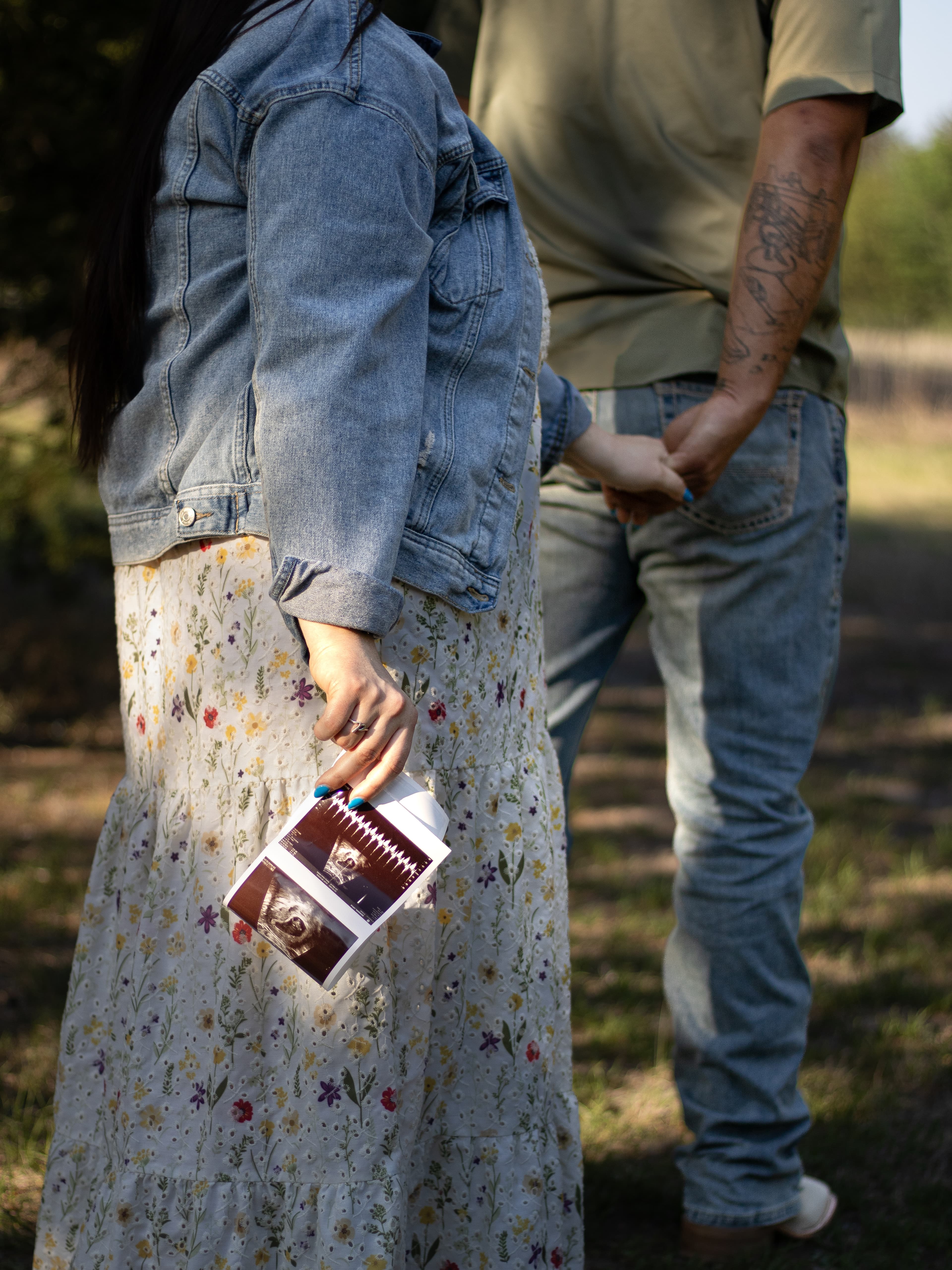 A close-up of an expectant couple holding hands and ultrasound photographs.