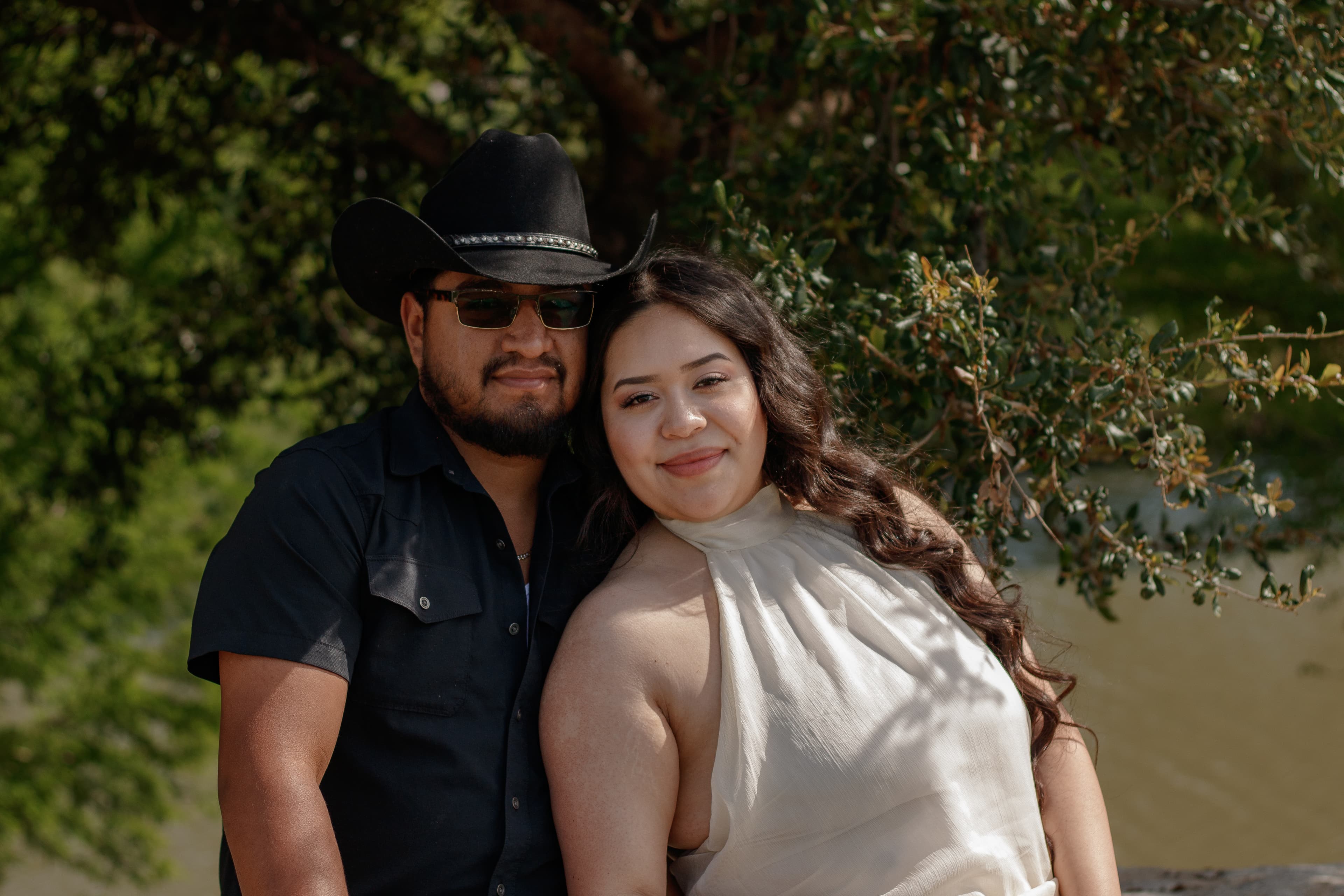 A couple leaning together beneath a leafy tree.