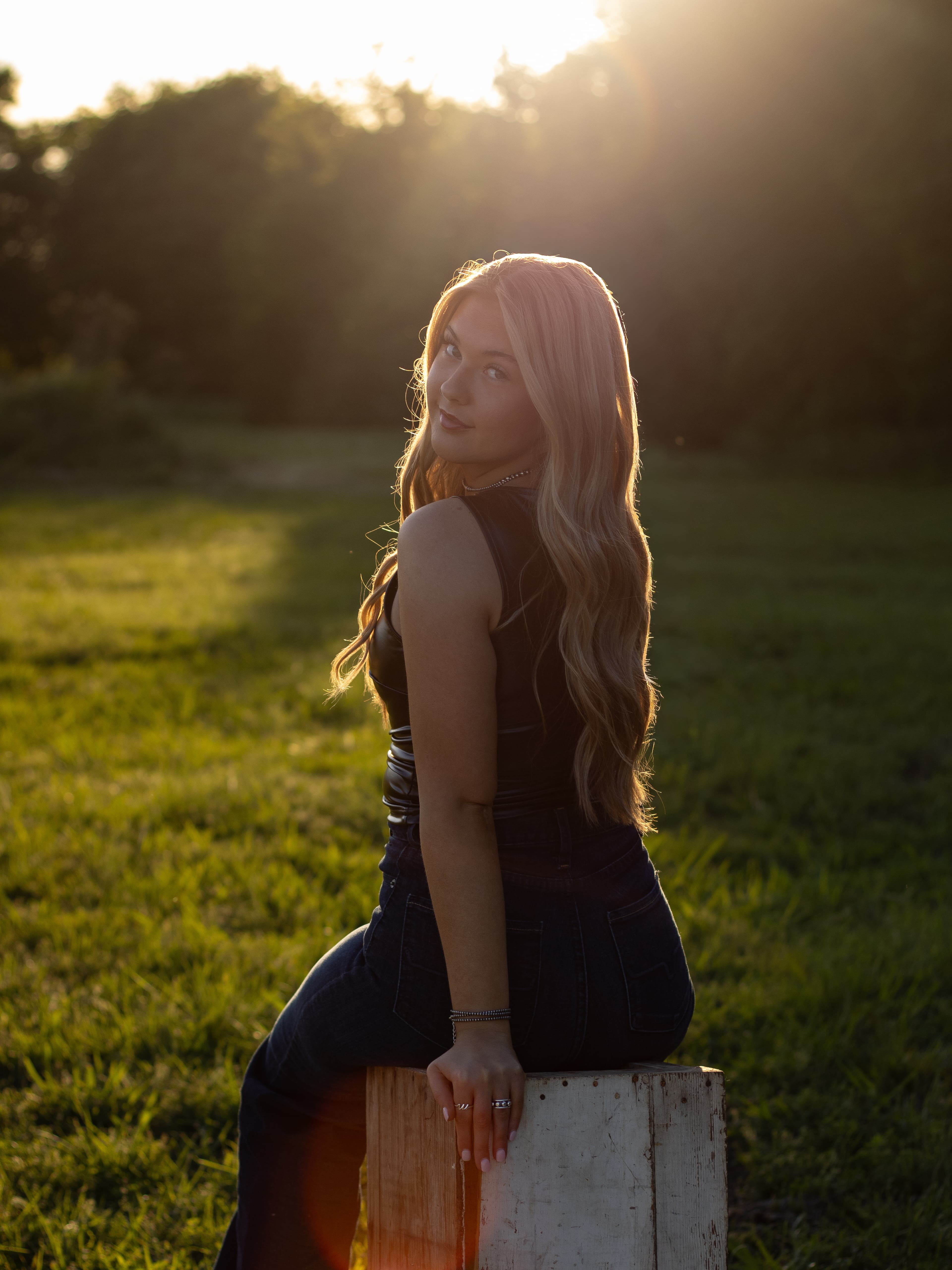 A woman seated in a field, looking over her shoulder in golden evening light.
